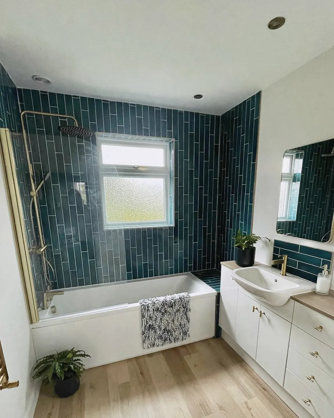 Bathroom with teal wall tiles, a brass shower over the bath and fitted vanity units