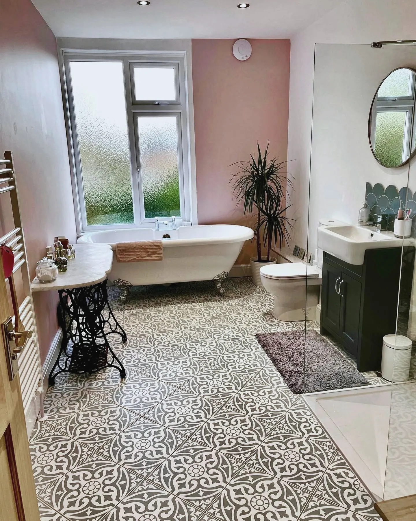 Bathroom with a roll-top bath beneath a window, pink walls and patterned floor tiles