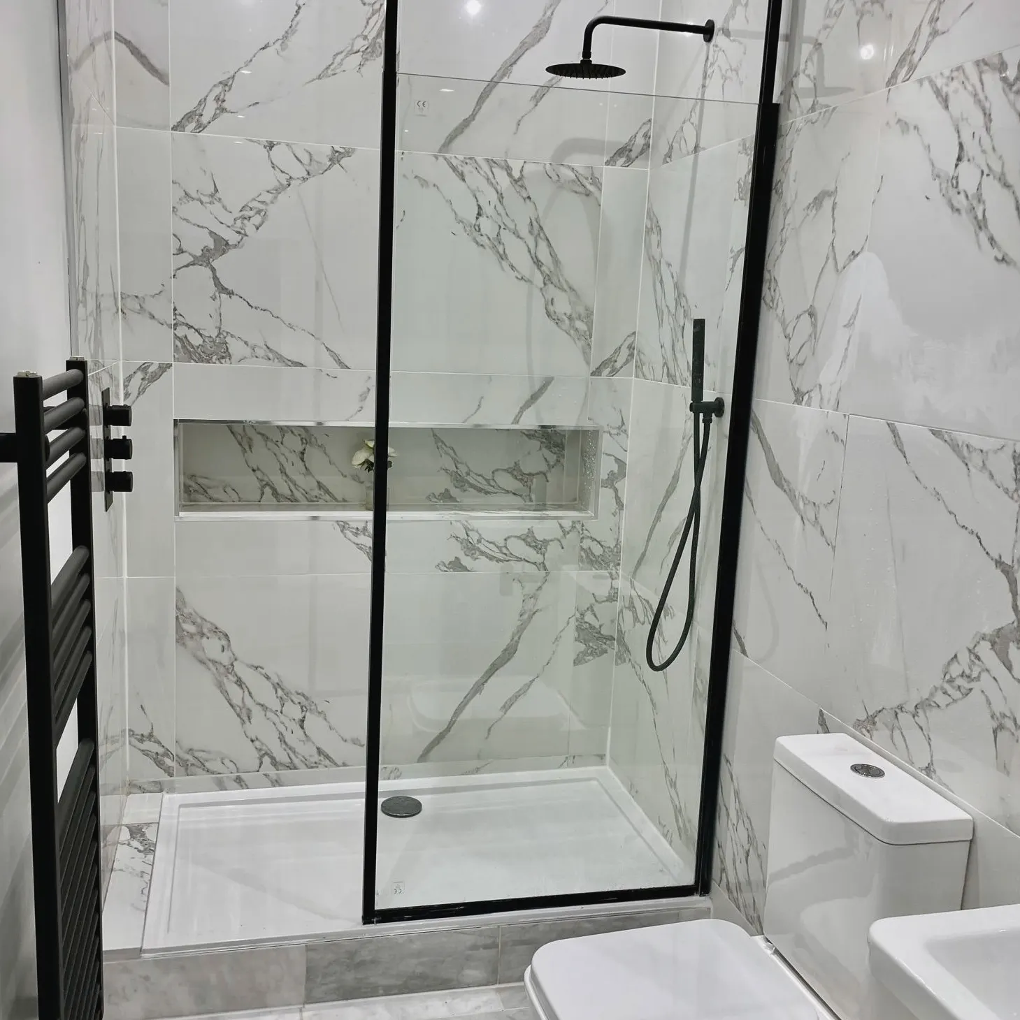 Walk-in shower with a black-framed screen, a recessed shelf and marble-effect tiles