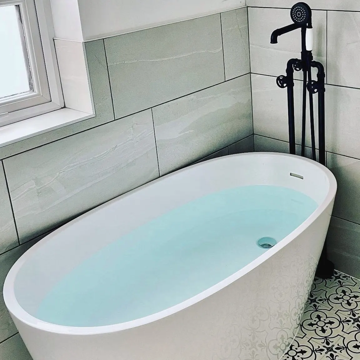 Freestanding bath filled from a black floor-standing tap, on patterned floor tiles